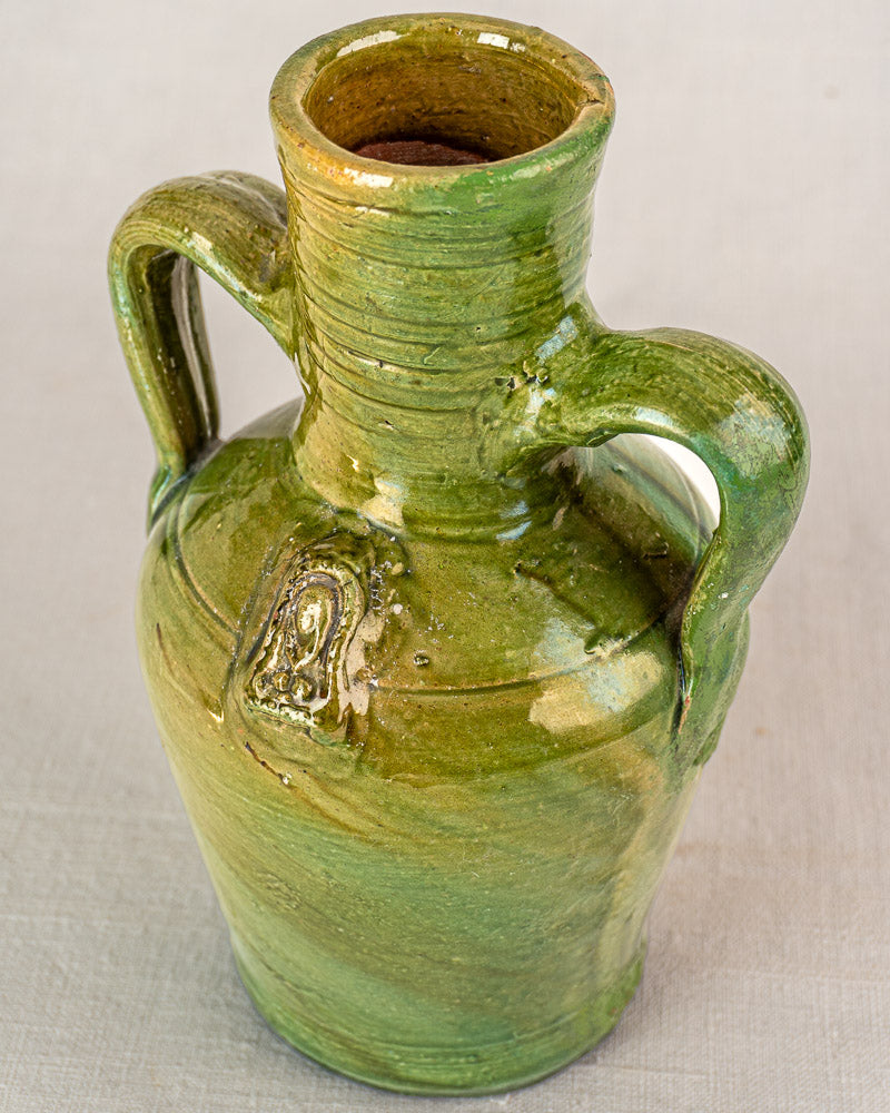 Green glazed French earthenware cruche with two handles, narrow neck, devotional medallion, and glossy Pyrenean finish.