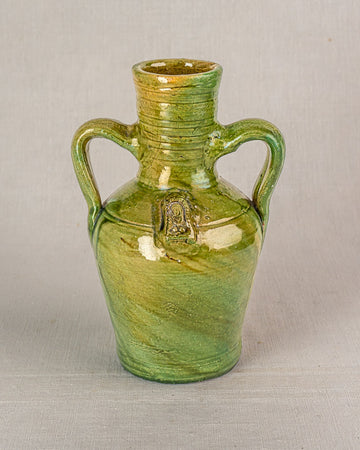 Antique French green glazed earthenware cruche with two handles and devotional medallion, on light gray background.