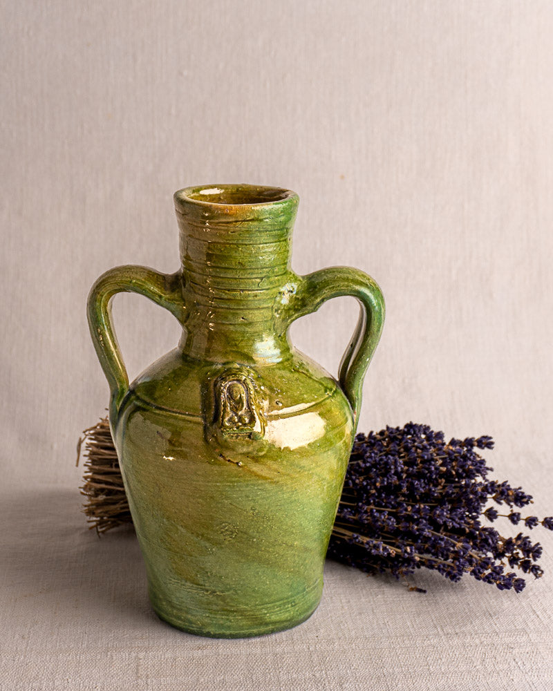 Antique French green glazed earthenware cruche with devotional medallion and two handles, dried lavender backdrop.