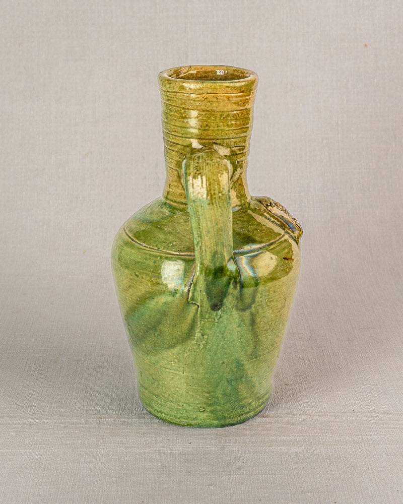 Antique French green-glazed earthenware cruche with wide neck, narrow spout, curved handle, and devotional medallion.