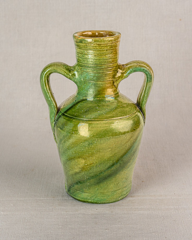 Antique French cruche in green glazed earthenware with spiral texture, dual handles, devotional medallion on gray woven fabric.