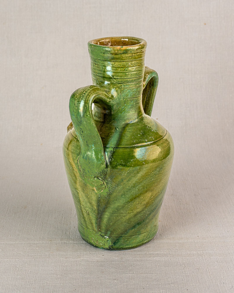 Green glazed antique French cruche jug with two handles, narrow neck, and devotional medallion on light background.