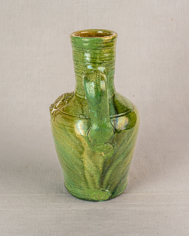Antique French green glazed earthenware cruche with single handle and devotional medallion, plain light gray background.