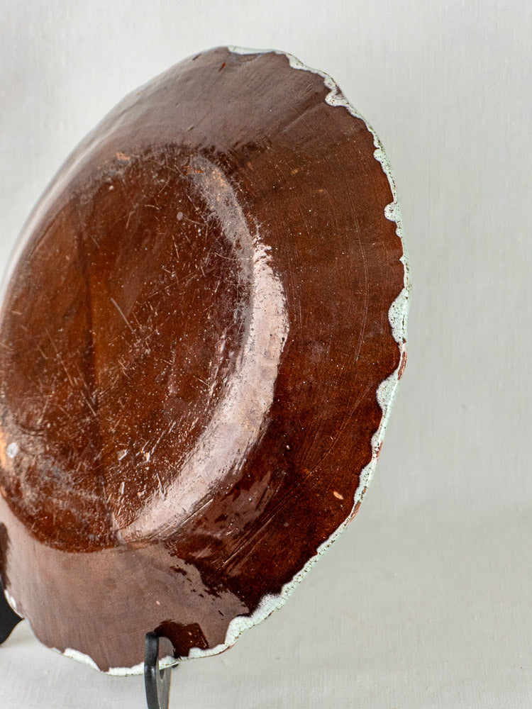 Back of round brown French faience charger with glossy finish, chipped edge, on stand.