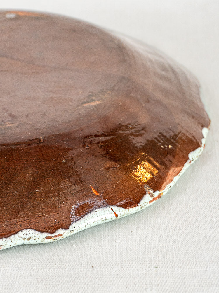 Underside of Cul Noir French faience charger with copper-toned glaze, chipped white edges on fabric.