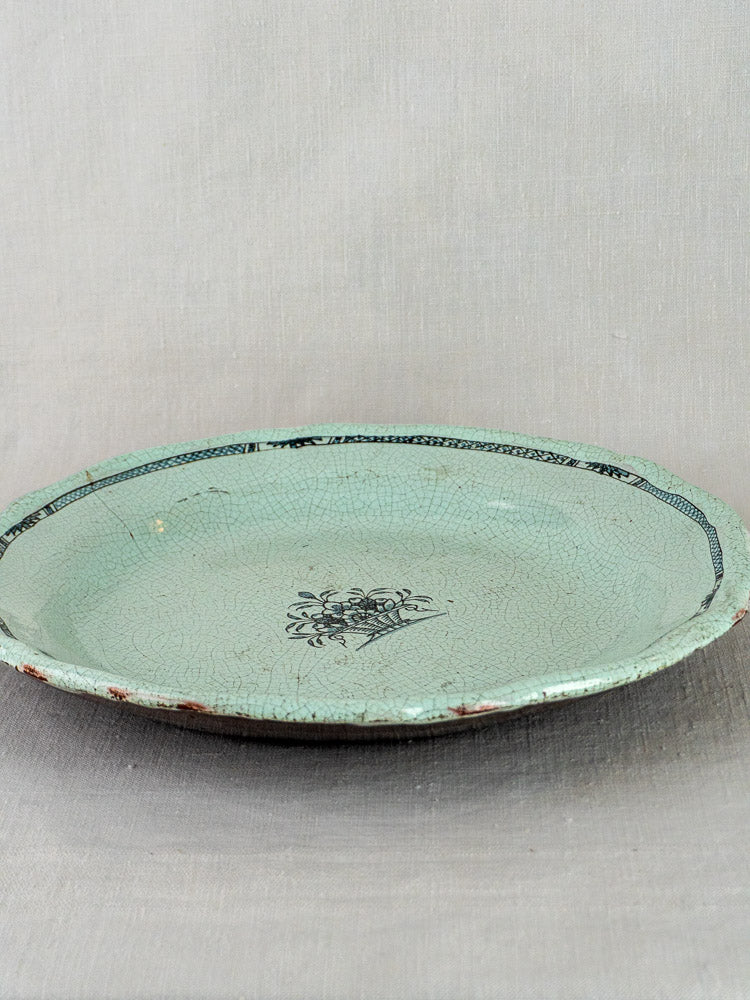 Antique French faience charger with celadon crackle glaze, floral center, and delicate border on fabric background.