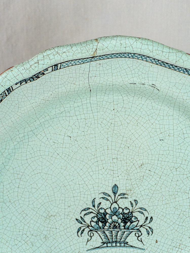 19th-century French faience charger with pale celadon glaze, black floral basket motif, and dark edge border.
