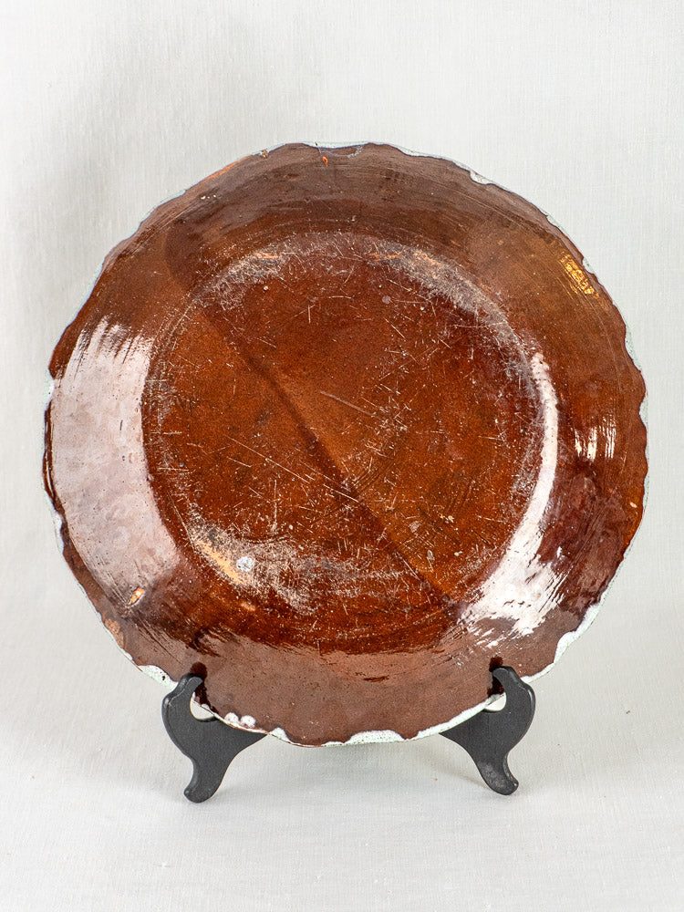 Large round French faience charger with celadon glaze, rustic brown tones, and scalloped edges on stand.