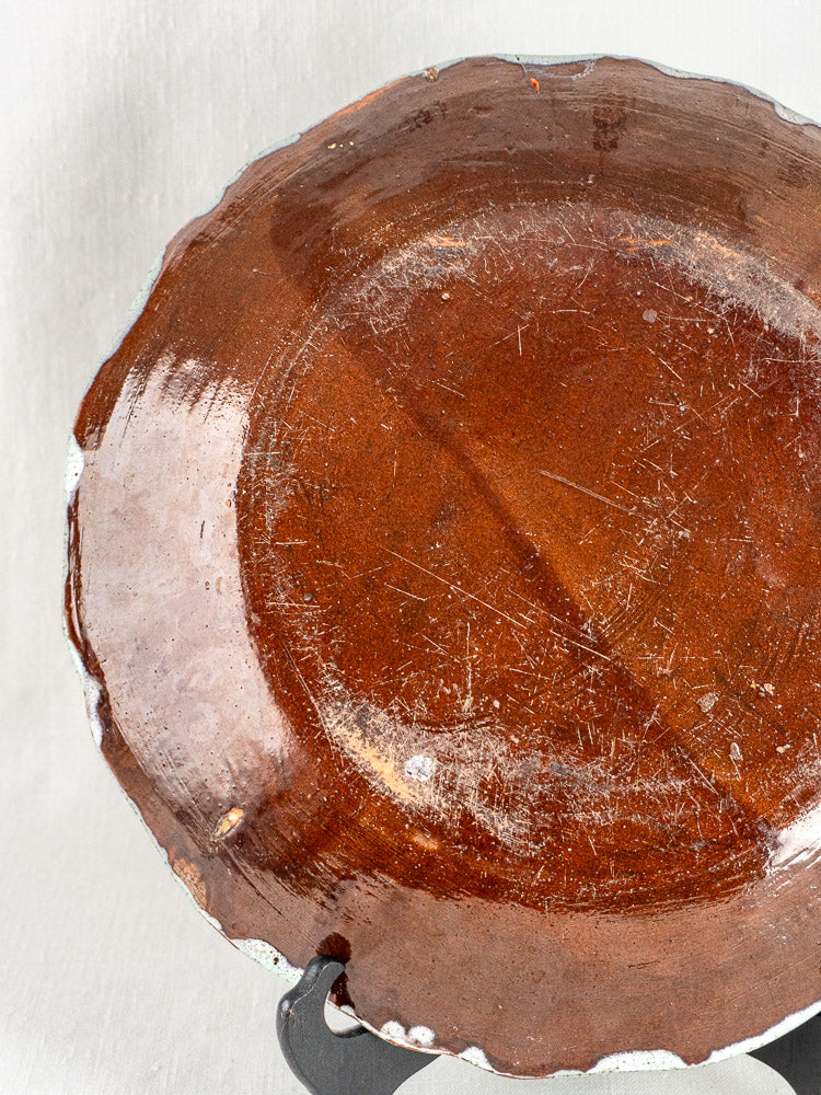 Antique French faience charger with brown glaze, glossy surface, and worn edges on black stand.