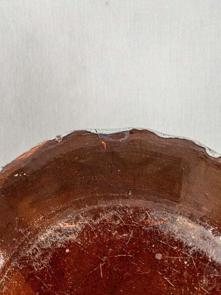 Antique French faience charger with celadon glaze, brown ceramic body, and worn, chipped edge.