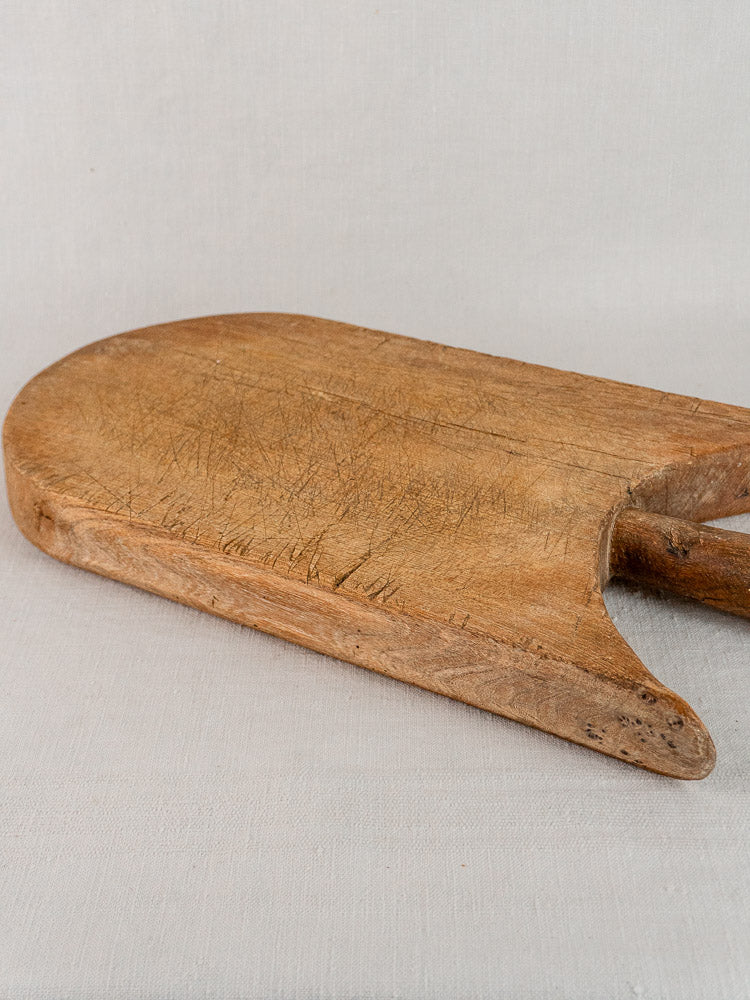 Antique French wing-shouldered cutting board with rounded end and knife marks on light fabric.
