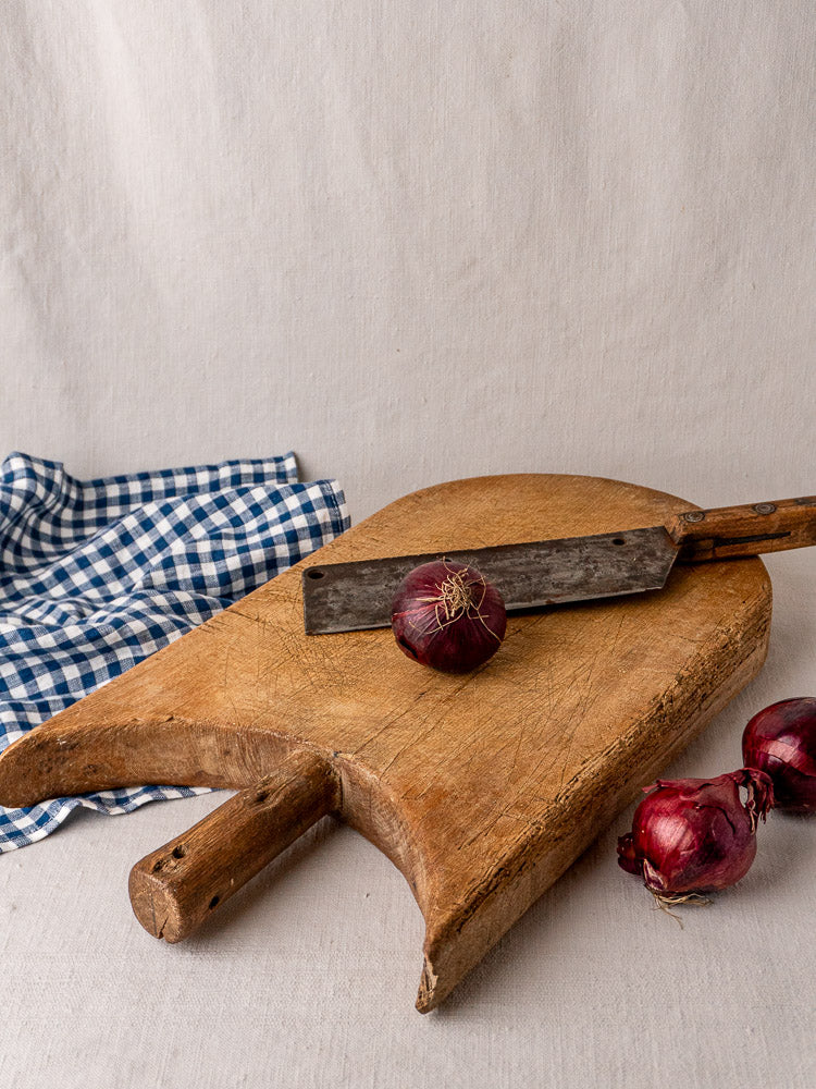 Antique French wing-shouldered wood cutting board with knife, red onions, and blue checkered cloth.