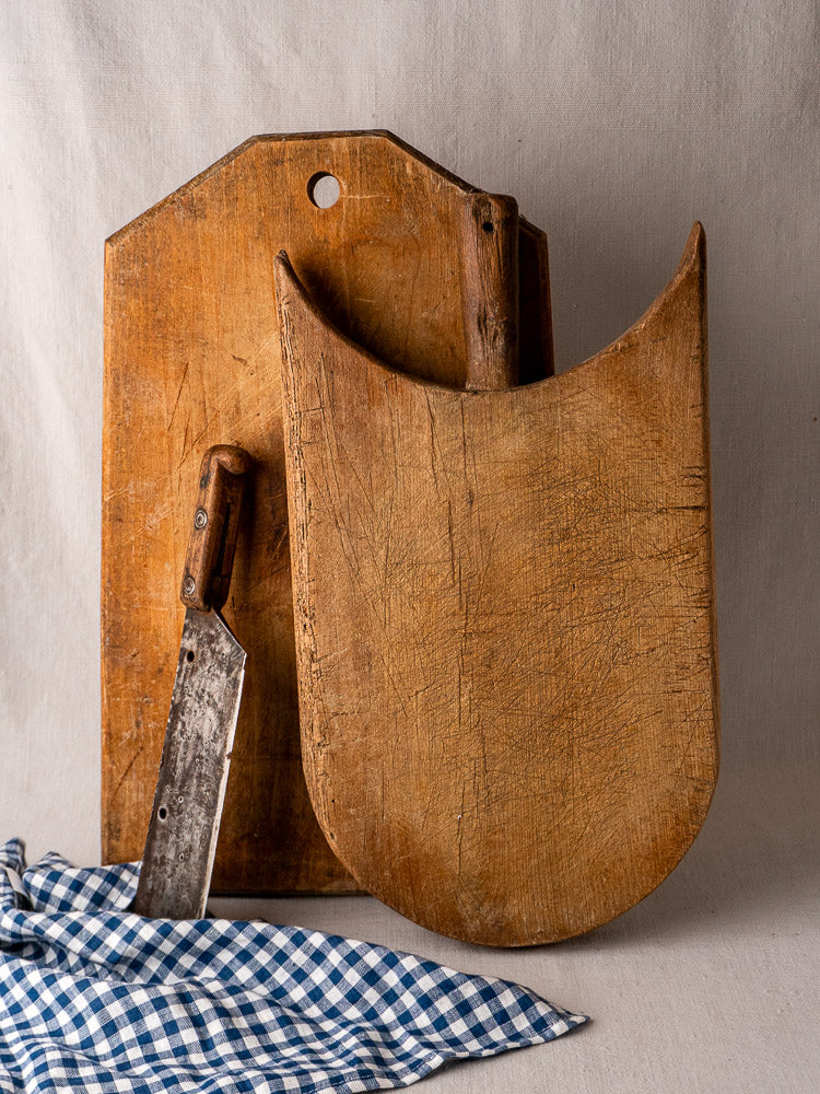 Antique French hand-carved wooden cutting board with vintage knife and blue checkered cloth.