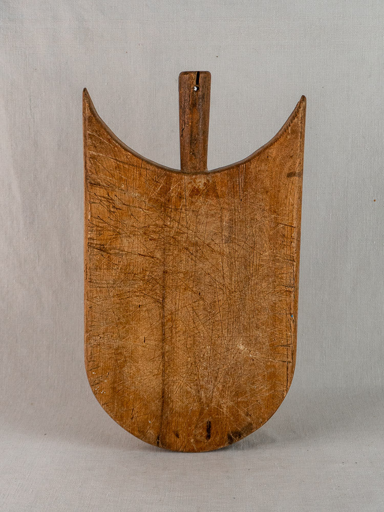 Antique French hand-carved wooden cutting board with rounded bottom, pointed sides, and visible knife marks.