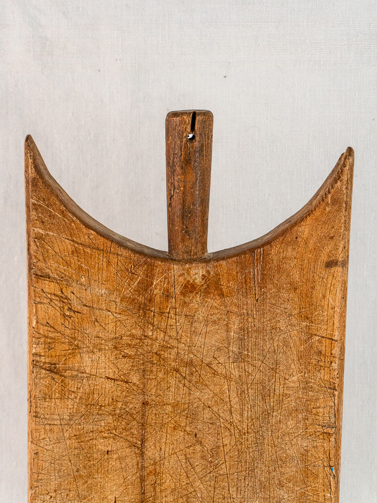 Antique French wing-shouldered wooden cutting board with U-shaped notch, showing timeworn texture against light background.