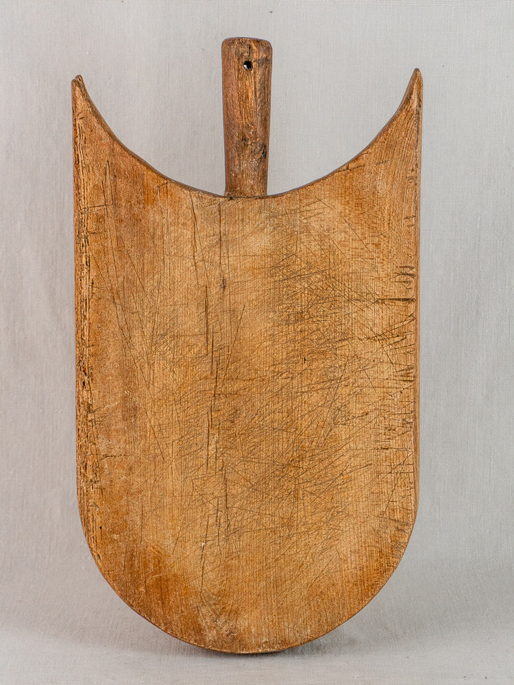 Antique French hand-carved wooden cutting board with winged shoulders and short handle, on light gray background.