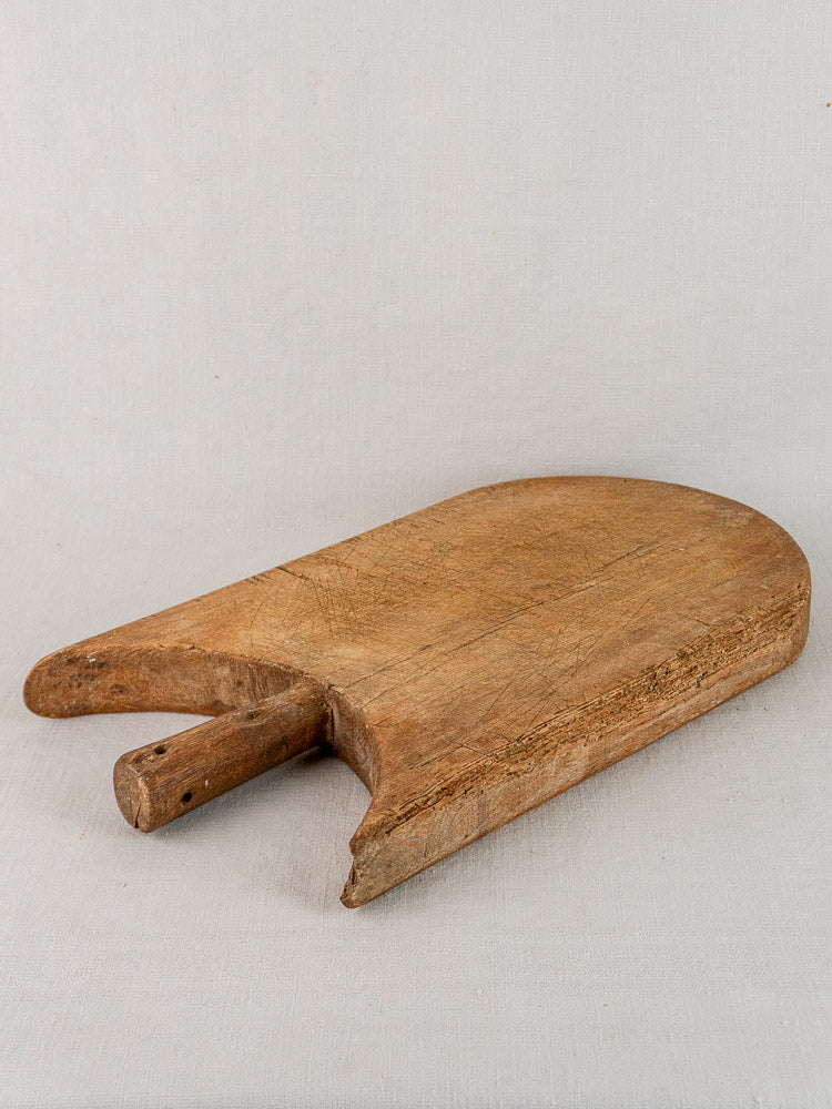 Antique French hand-carved cutting board with rounded edge and dual prongs on light fabric surface.