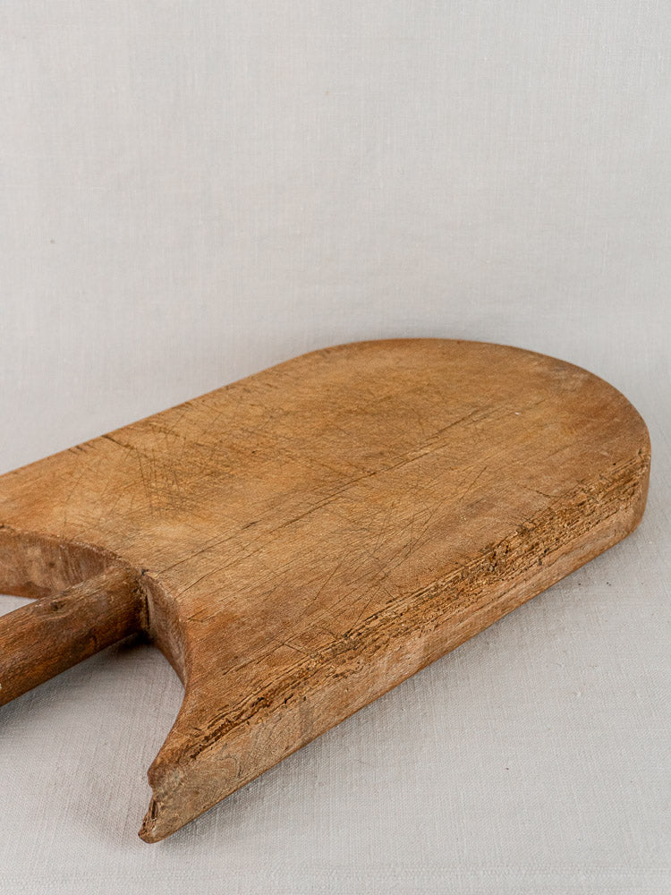 Antique French wing-shouldered wooden cutting board with worn patina on a light beige surface.