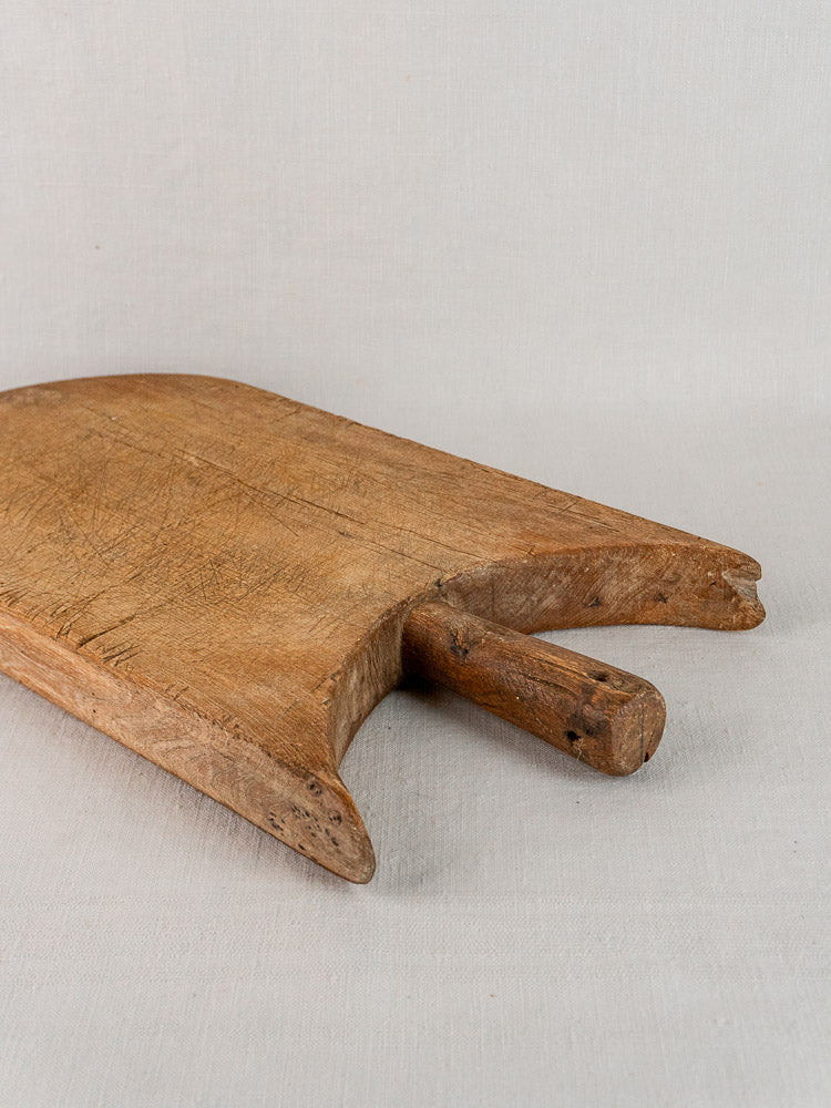 Antique French wing-shouldered wood cutting board with cylindrical handle on light fabric background.