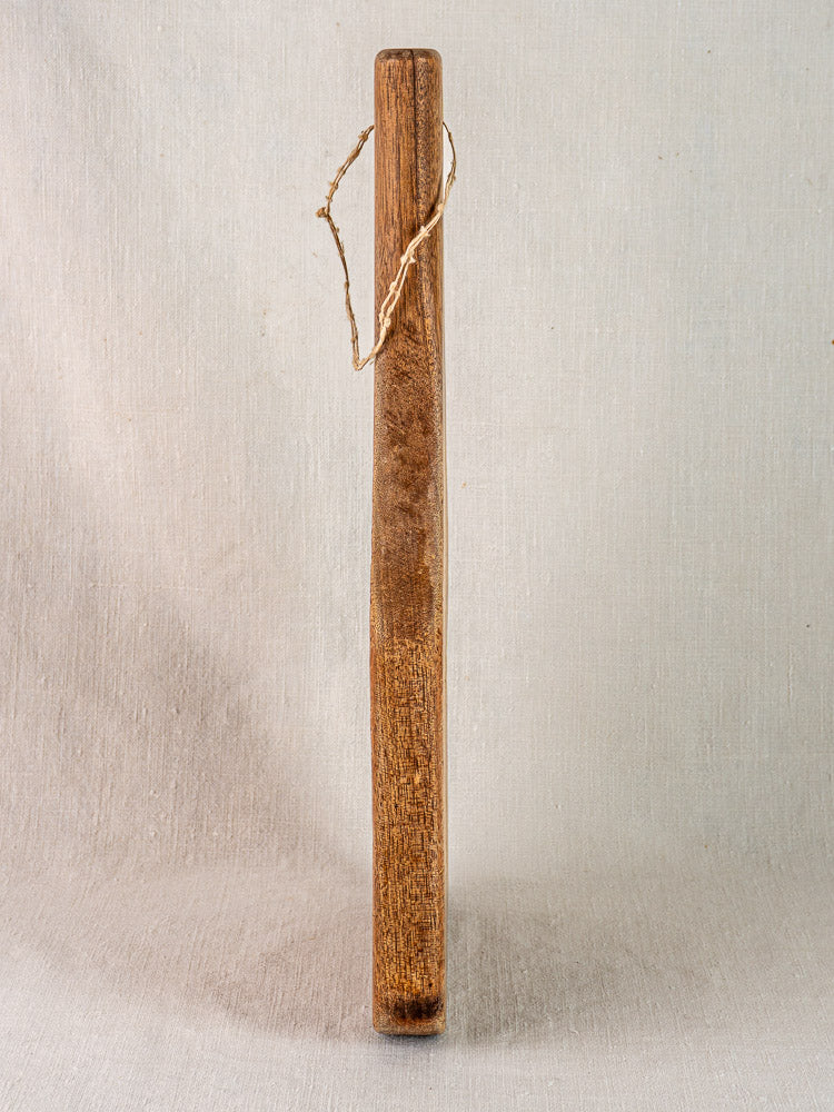 Hand carved antique French chestnut cutting board with tapered handle on a white fabric backdrop.