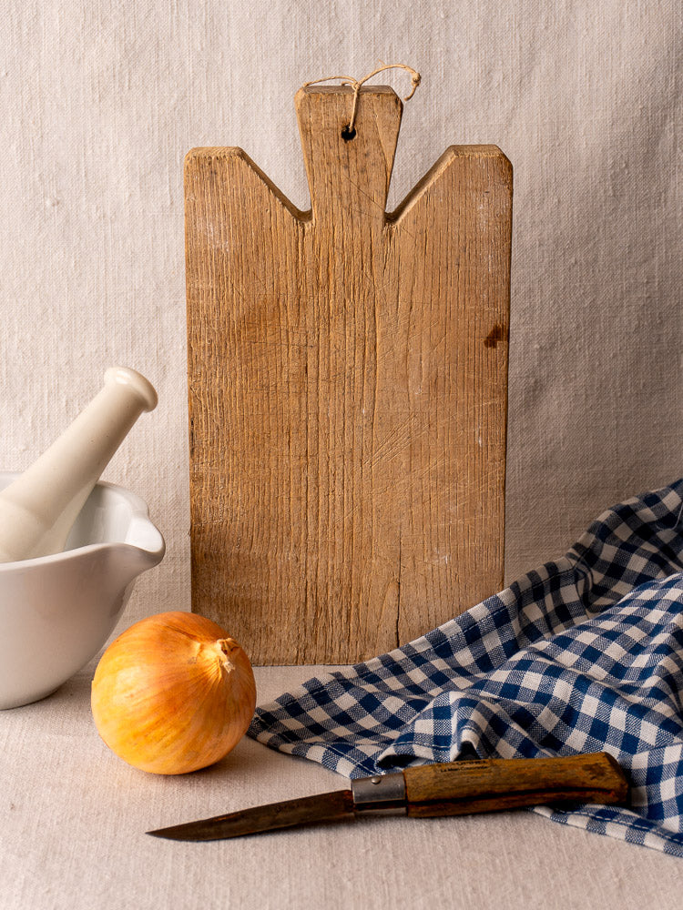 Antique French oak cutting board, late 19th century, with mortar, onion, paring knife, and checked cloth.