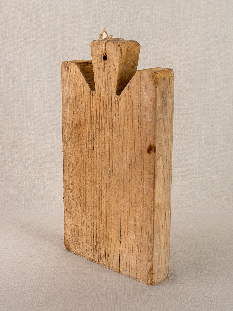 Late 19th-century French oak cutting board, thick rectangular form with top notch and string loop, upright on light fabric backdrop.