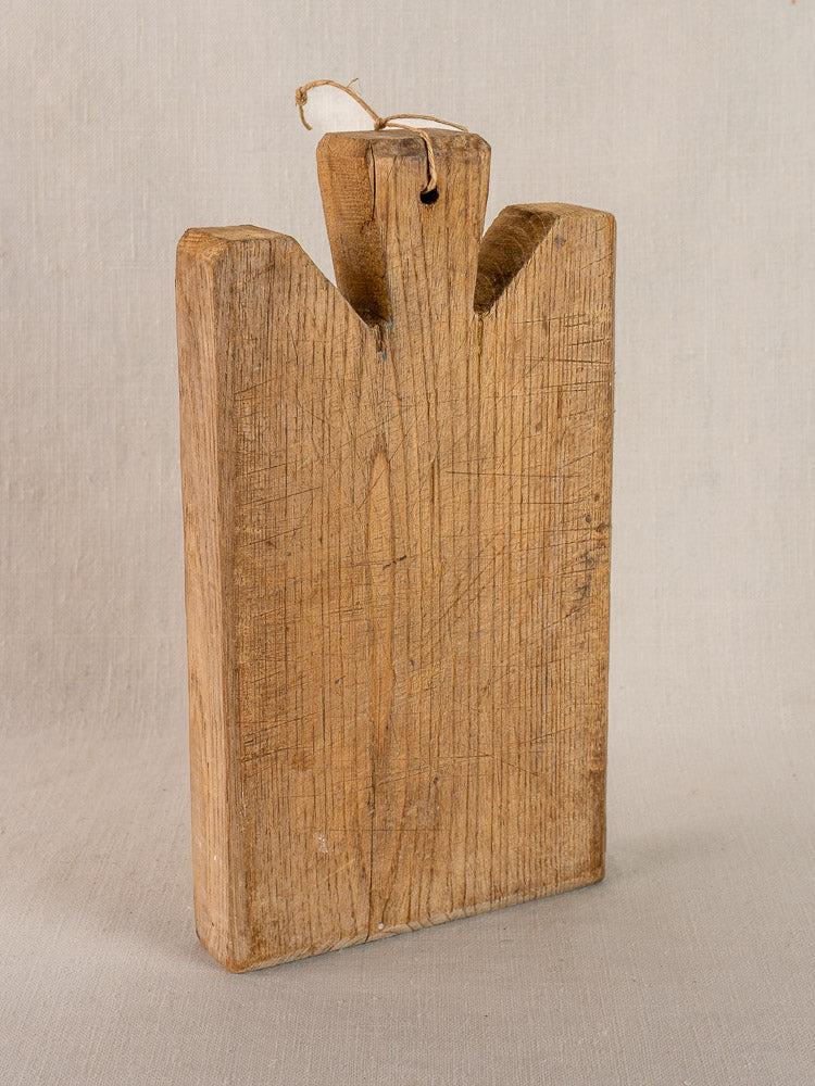 Antique French hand-carved oak cutting board, vertical rectangular shape, top handle with string, visible wood grain, rustic wear.
