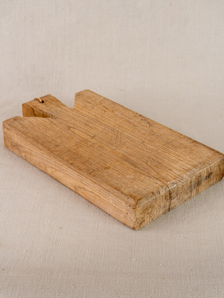 Antique French oak cutting board with notched handle and aged patina on a light textured surface.