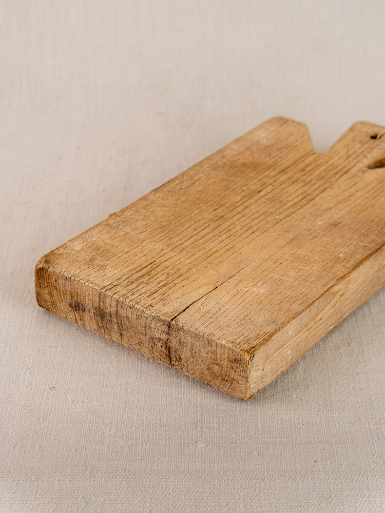 Antique French oak cutting board with visible grain and rustic patina on a light beige fabric surface.
