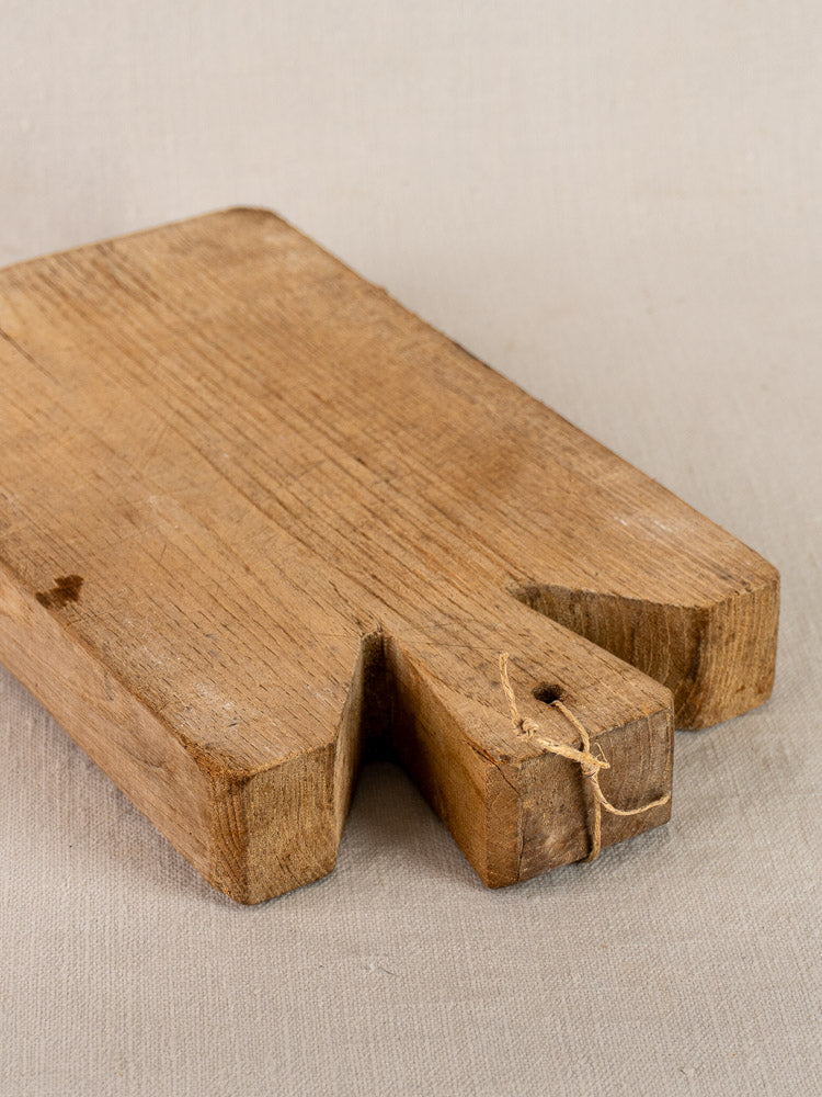 Antique French oak cutting board, hand-carved with notched edge and twine tie on neutral fabric surface.