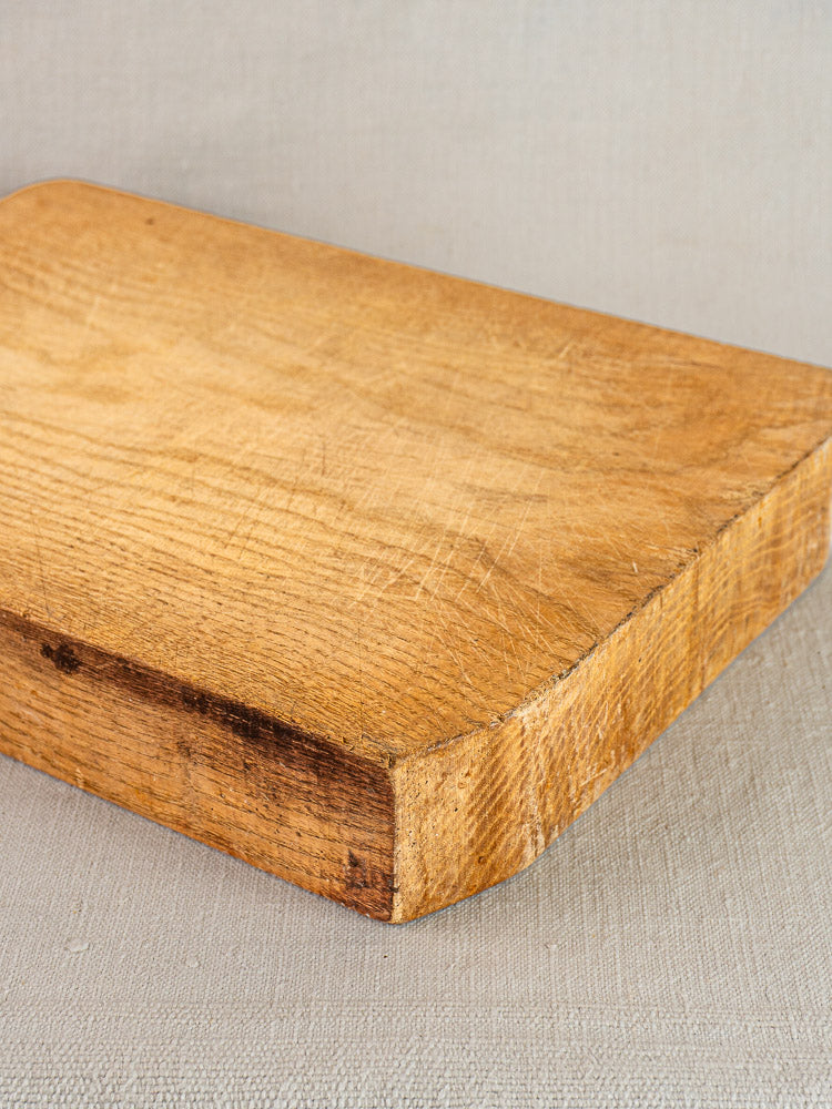 Antique French hand-carved wood cutting board with rounded corners and textured, scratch-marked surface on light fabric.