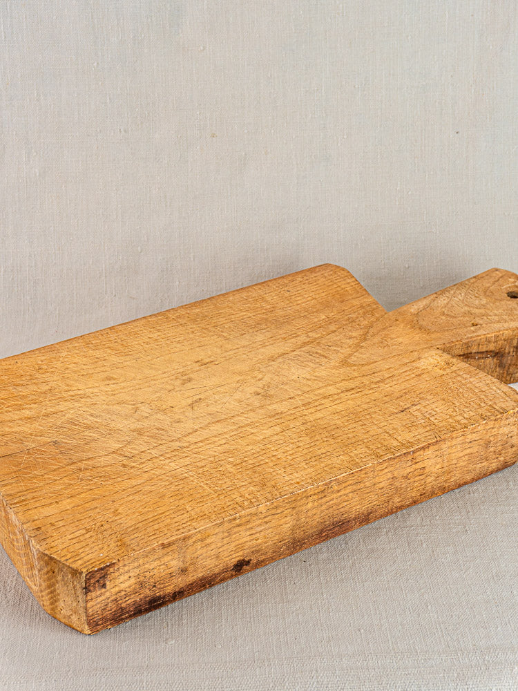Antique French hand-carved cutting board with handle and hanging hole on a light grey textured surface.