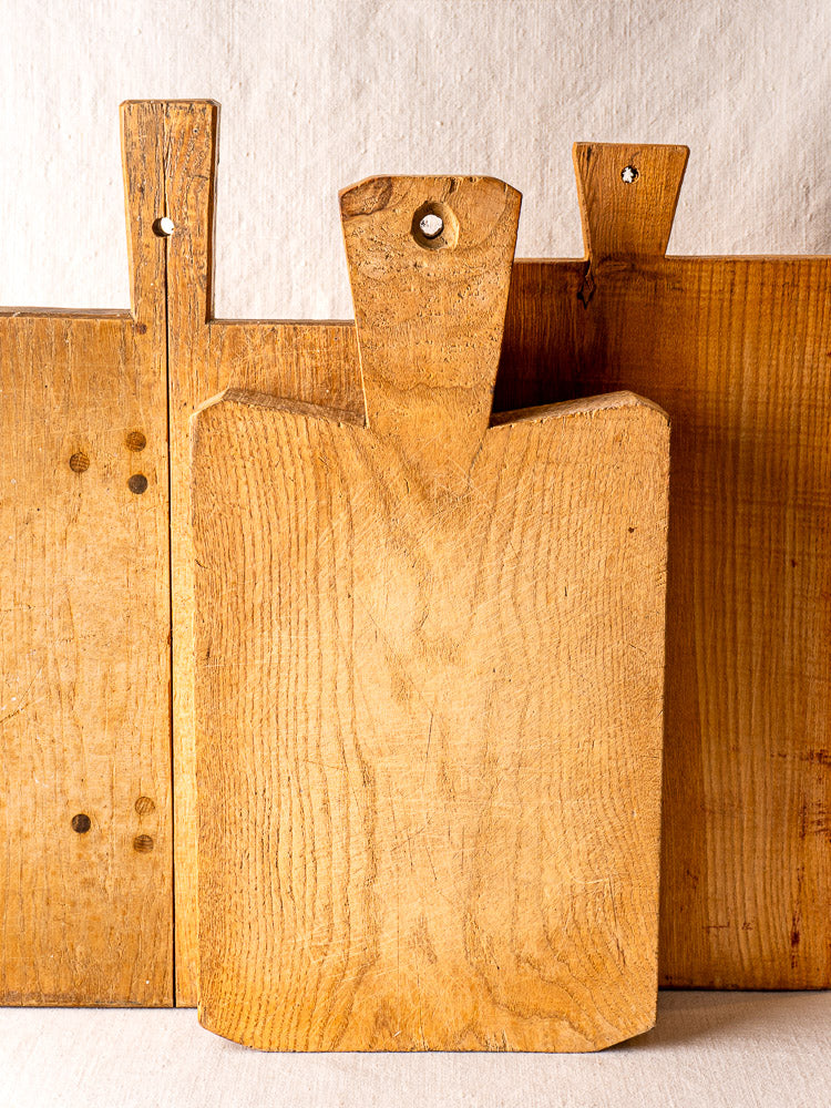 Set of three antique French cutting boards, hand-carved thick wood, visible grain and handle holes, upright on neutral background.