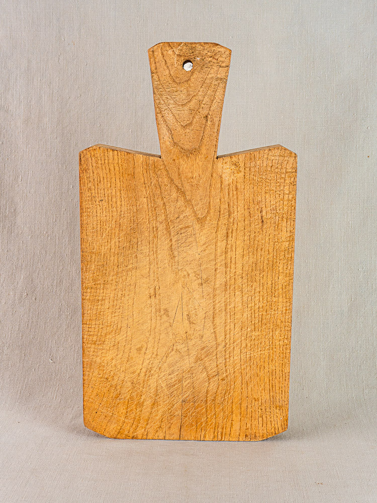 Antique French cutting board, hand-carved thick wood, displayed upright against a textured background.