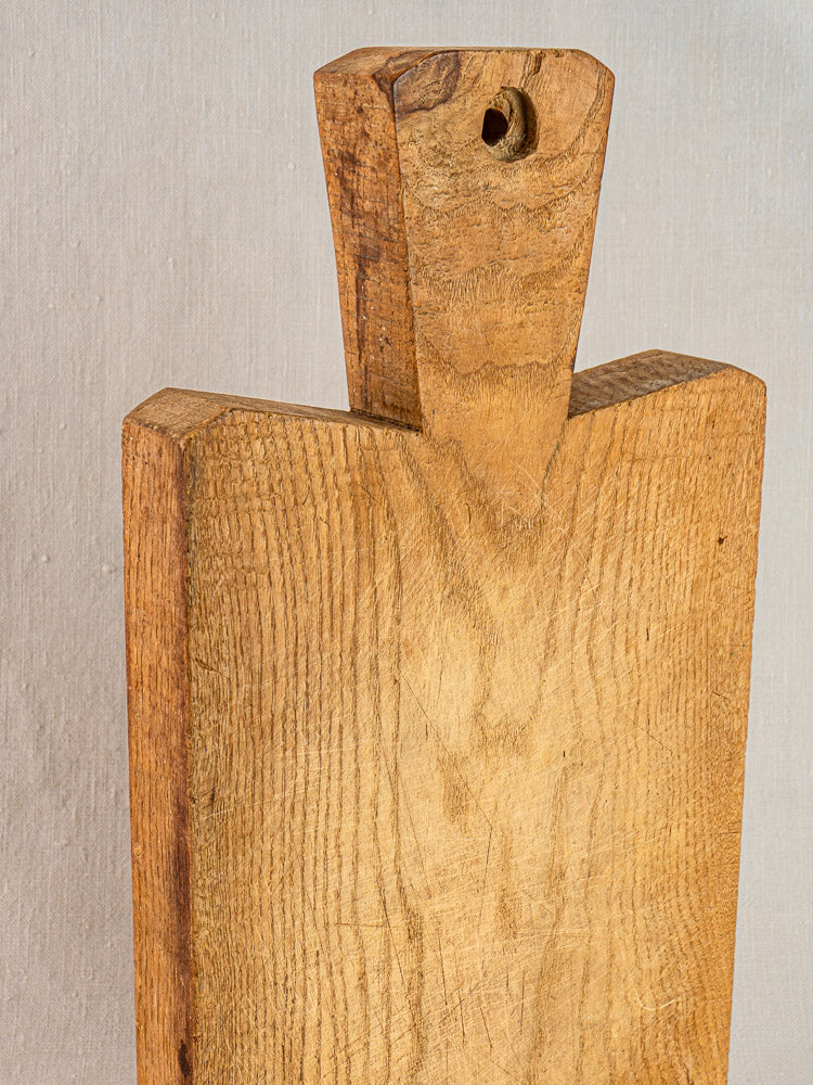 Antique French hand-carved wood cutting board with handle and top hole, rich grain showing, set on a light background.