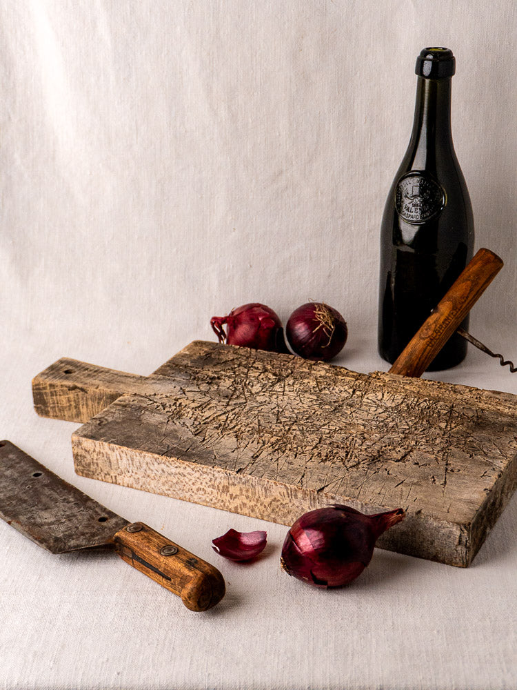 Late 19th-century French antique wooden cutting board with handle, upright against a plain background.