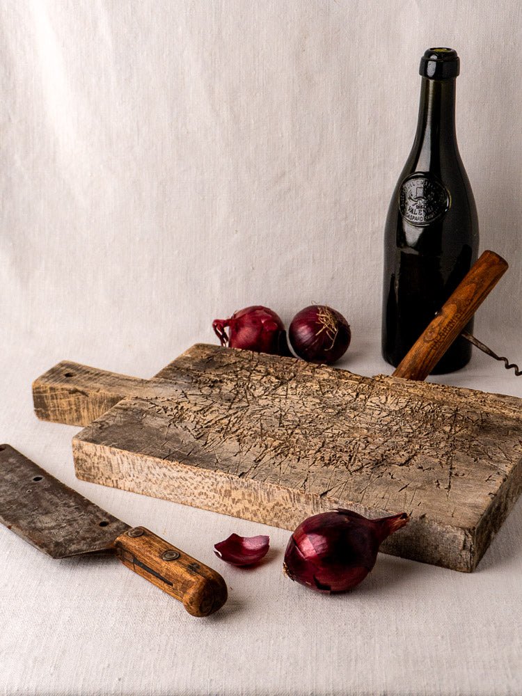 Antique French solid wood cutting board, late 19th century, with knife, onions, wine bottle, corkscrew on light cloth.