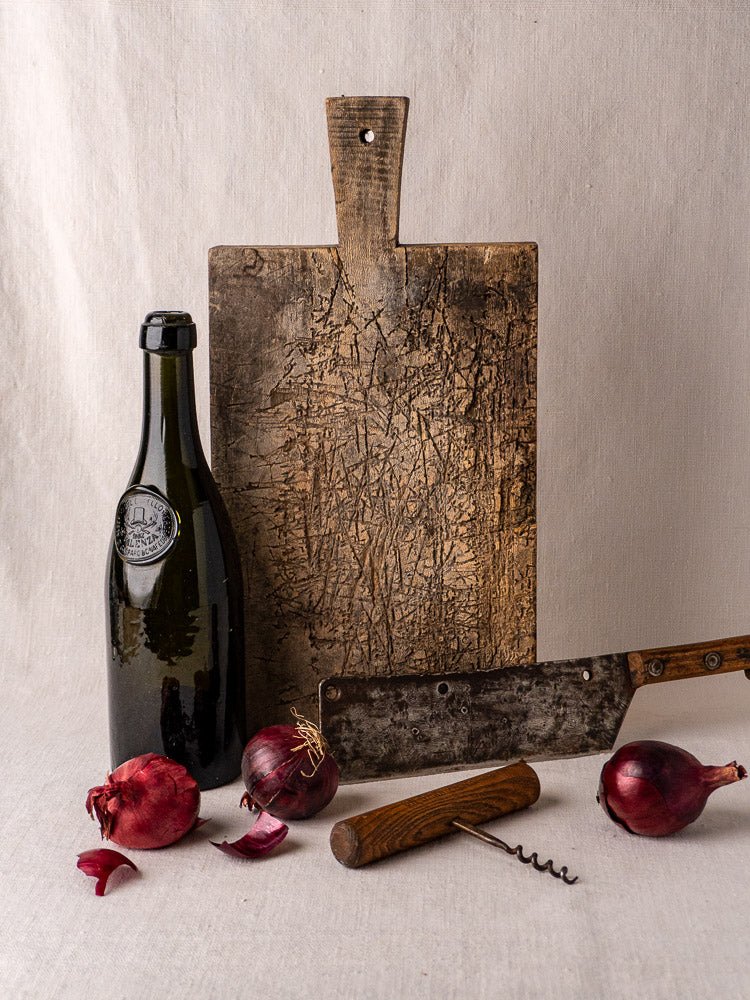 Late 19th century French solid wood cutting board displayed with wine bottle and red onions.
