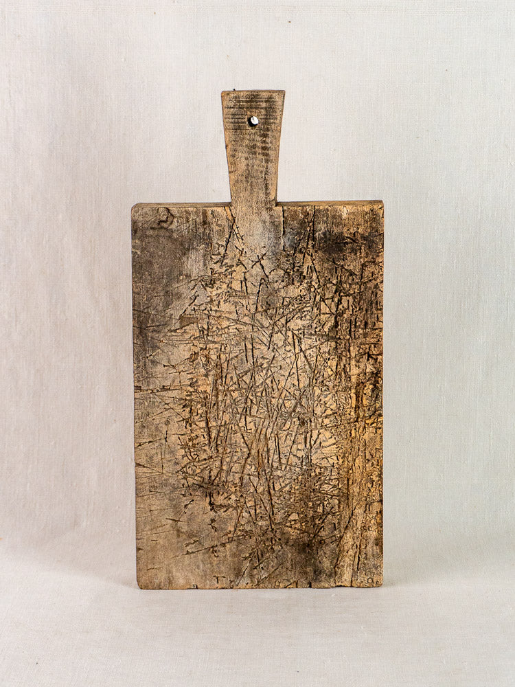 Late 19th-century French antique wooden cutting board with handle, upright against a plain background.