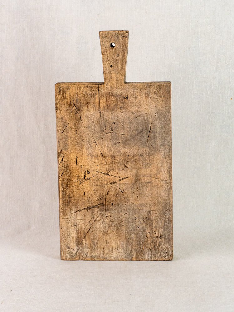 Late 19th-century French antique wood cutting board with handle and top hole, on light background.