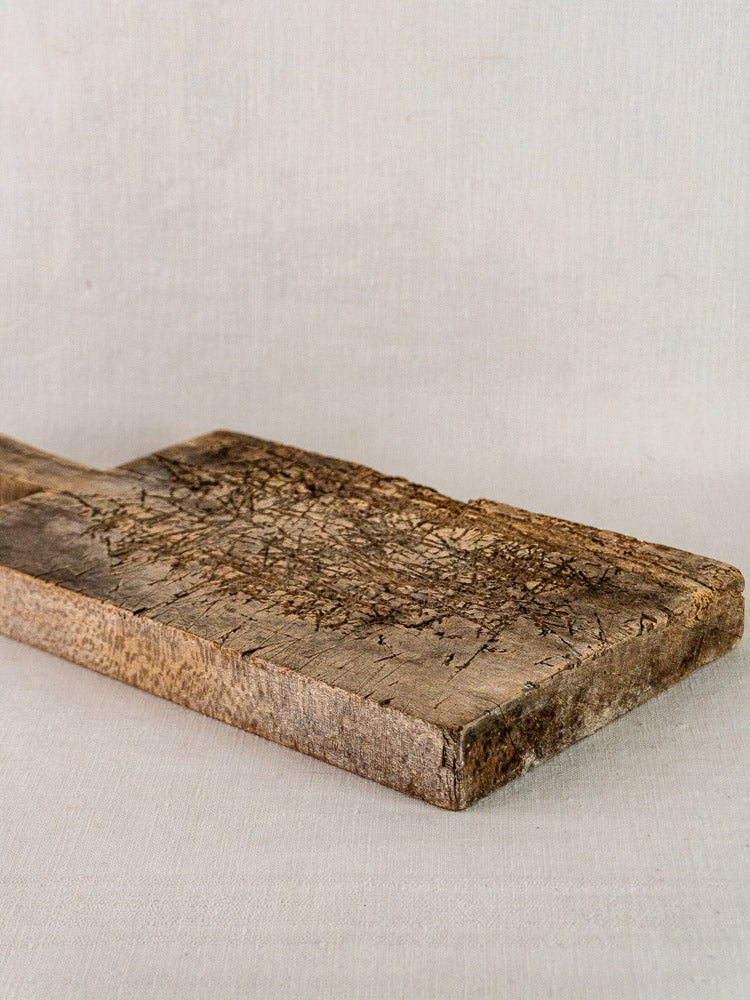 Antique French solid wood cutting board with weathered texture and cracks on light fabric background.