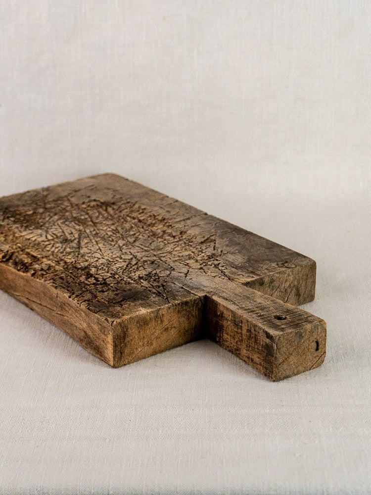 Antique French solid wood cutting board with deep knife marks and patina on fabric background.