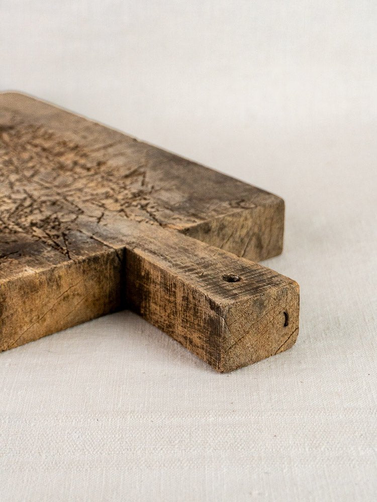 Antique French solid wood cutting board, late 19th century, corner and handle in focus on light fabric.