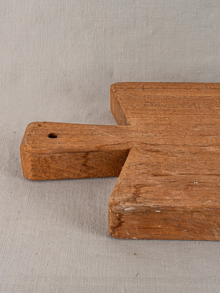 Antique French hardwood cutting board with handle and hole, early 20th century, on light gray textured surface.