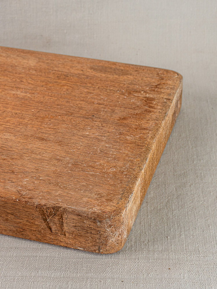 Antique French hardwood cutting board with rounded edges on a light gray textured fabric background.