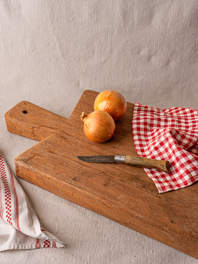 Antique French cutting board, hand-finished hardwood, early 20th century, with onions, knife, and checkered cloth.