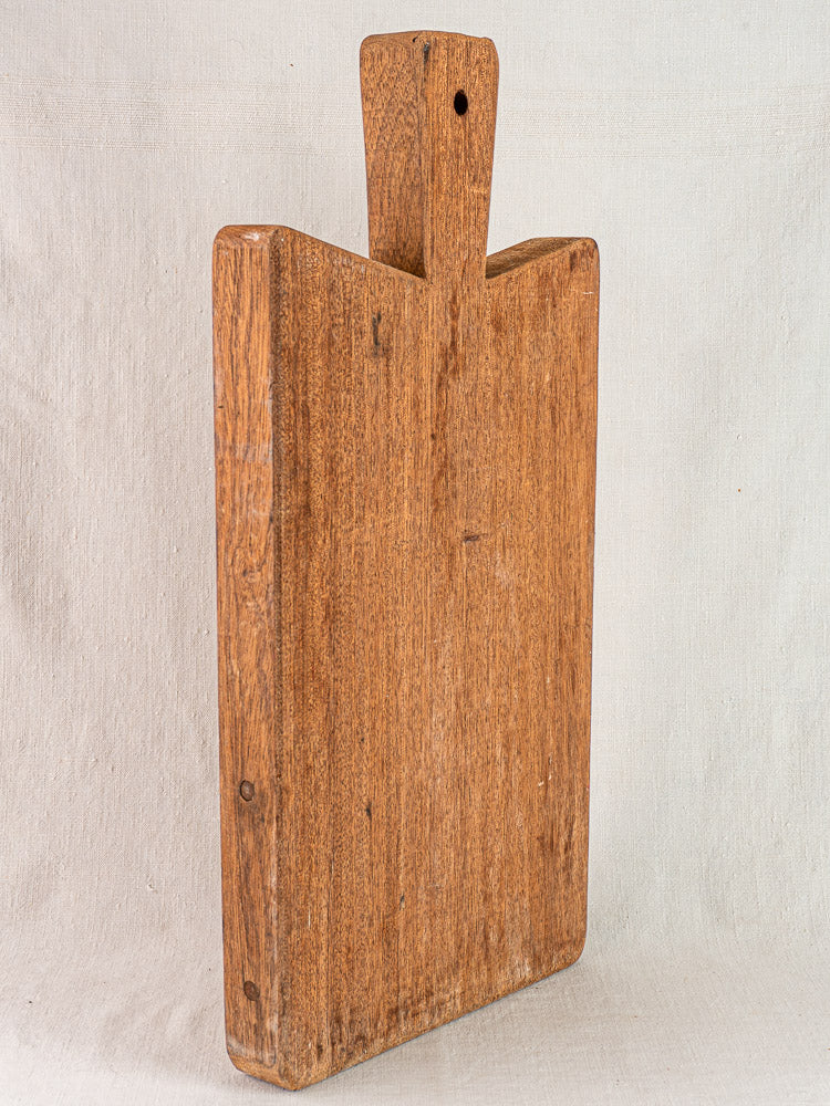 Antique French hardwood cutting board with hand-finished details, upright on a light textured surface, rustic vintage charm.