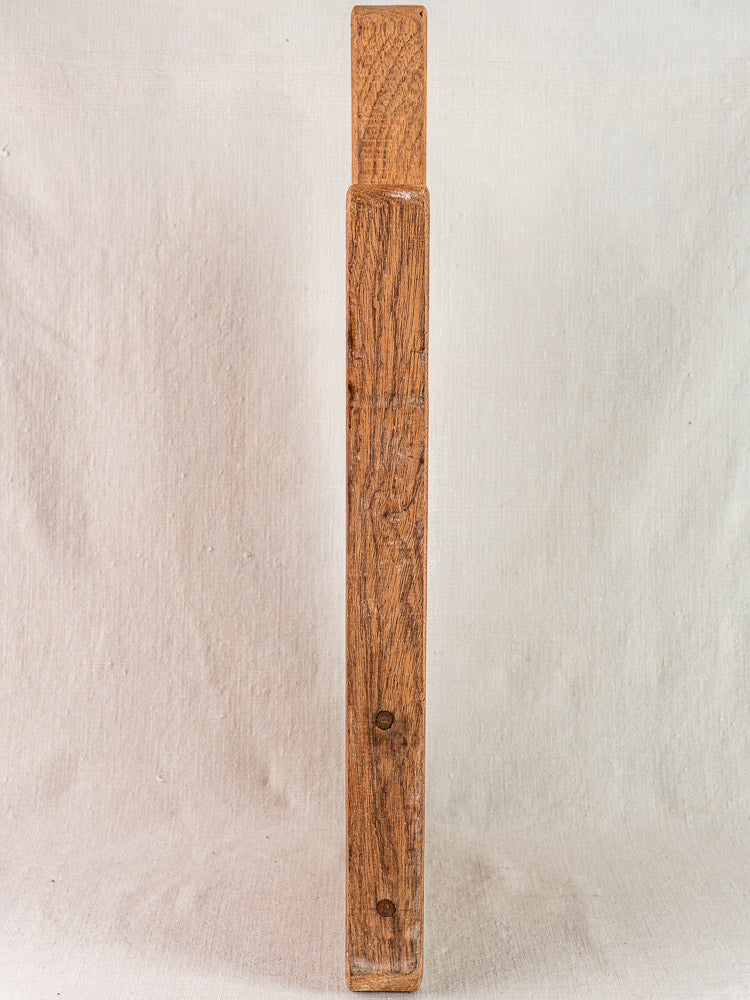 Antique French hardwood cutting board, tall and narrow with visible grain, two screw holes, upright on textured light surface.