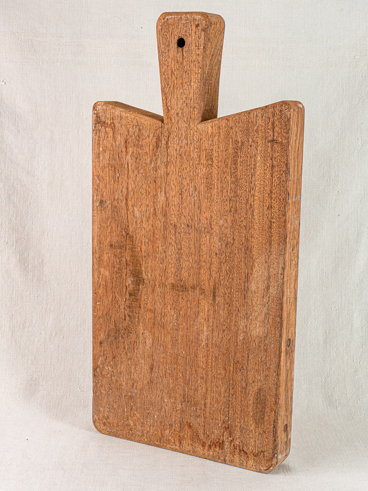 Antique French hardwood cutting board, early 20th century, rectangular with handle, upright on a light background.