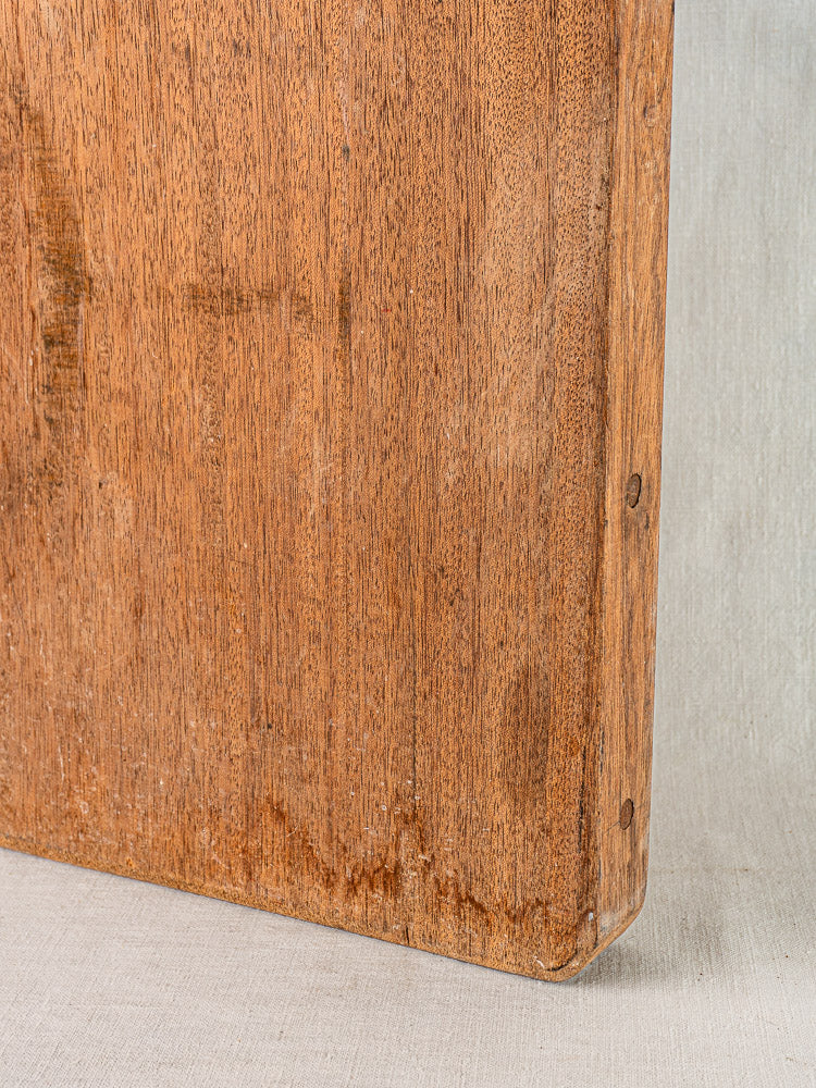 Antique French cutting board in hand-finished hardwood with visible grain and rounded edges on light fabric.